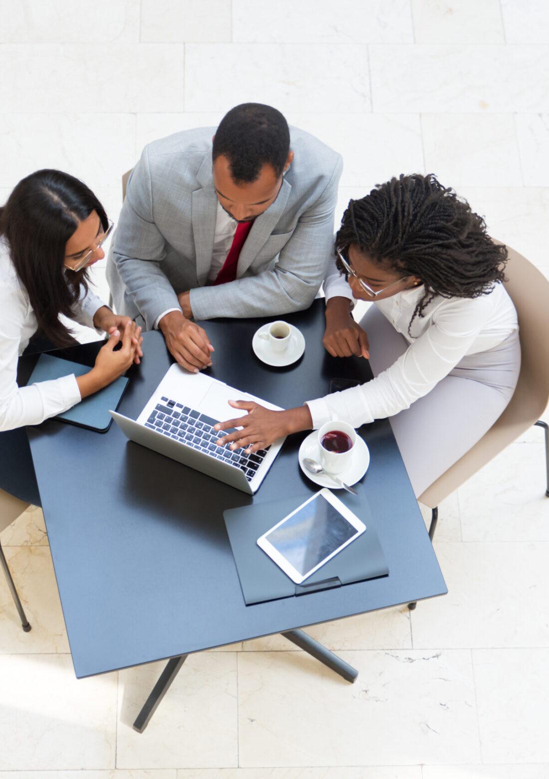 Business colleagues watching content on laptop while drinking coffee. Business man and women sitting at table with tablet, working on computer, looking at screen. Wireless communication concept